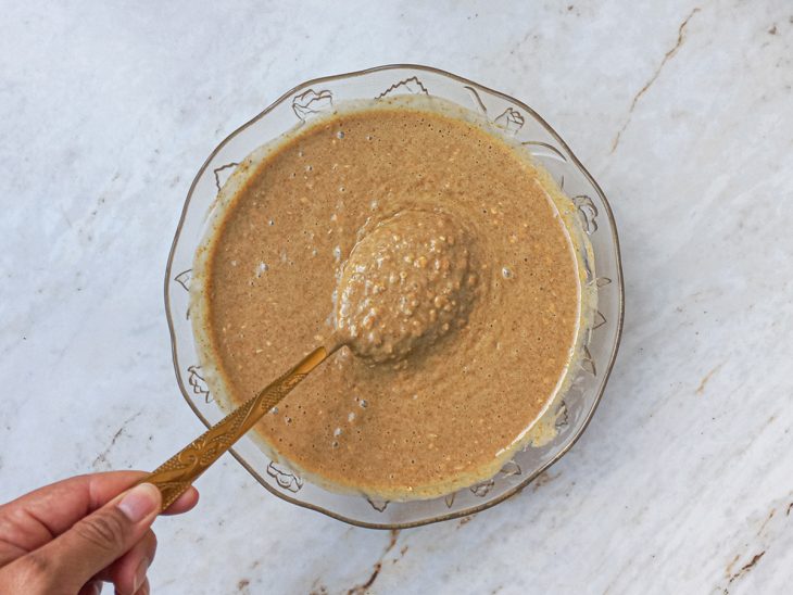 Mistura do liquidificador agregada a mistura de ingredientes secos no recipiente de vidro.