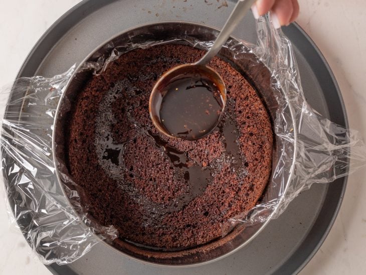 Disco de bolo sendo umedecido com calda de chocolate.