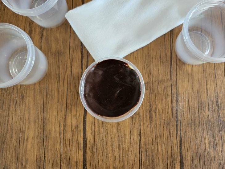 Um pote forrado com creme branco e coberto com pedaços de chocolate, creme e coberto com ganache.