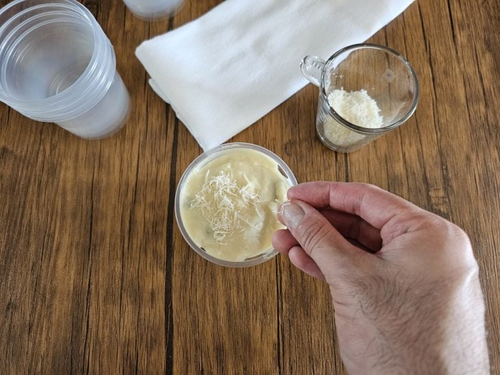 Um pote forrado com creme branco e coberto com pedaços de chocolate, creme e coco ralado.