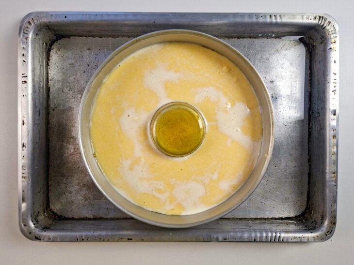 Pudim sendo despejado delicadamente sobre a massa do bolo dentro da forma.