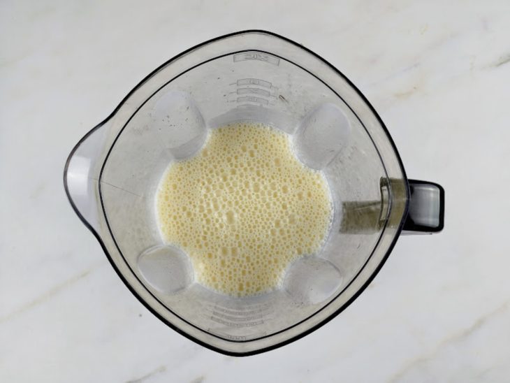 Um liquidificador com ovos, óleo, leite de coco e açúcar batidos.