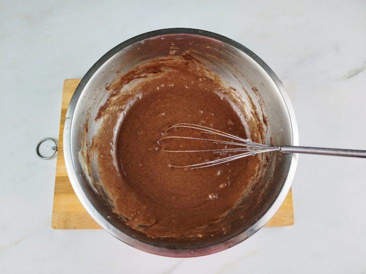Ingredientes batidos com um fouet em uma tigela redonda de inox.