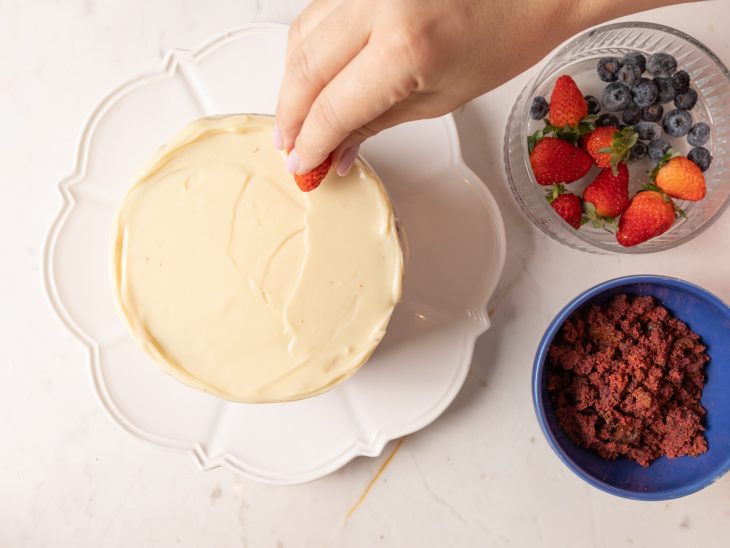 Bolo red velvet coberto por creme e com frutas vermelhas para adicionar.