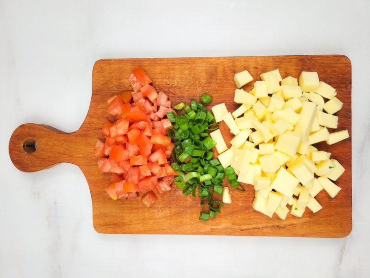 Tomate, cebolinha e mussarela picados em cima de uma tábua.