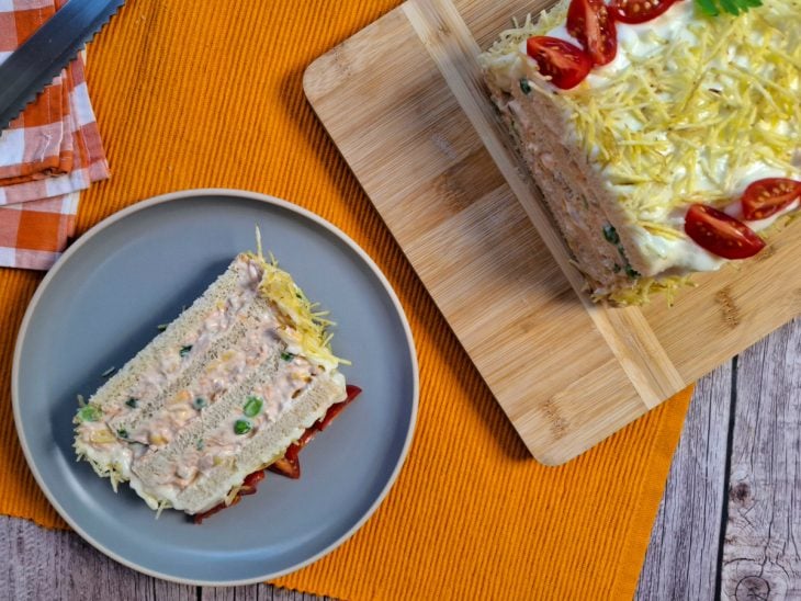 Bolo salgado de atum pronto em uma tábua e fata servida em um prato redondo individual.
