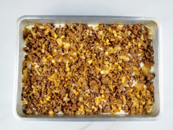 Camadas de massa e recheio de carne moída em uma forma untada.