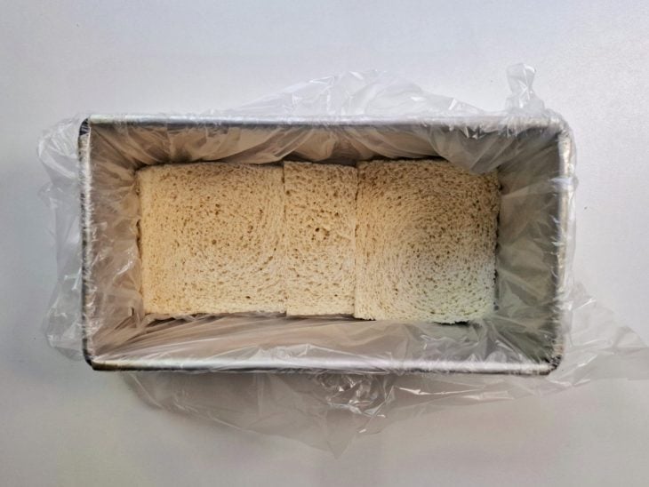 Forma forrada com plástico e com uma camada de pão de forma ao fundo.