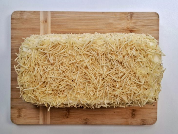 Fina camada de maionese e batata-palha salpicada sobre todo o bolo.