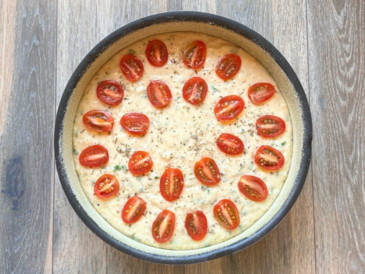 Massa despejada na assadeira untada e decorada com tomates-cereja cortados ao meio.