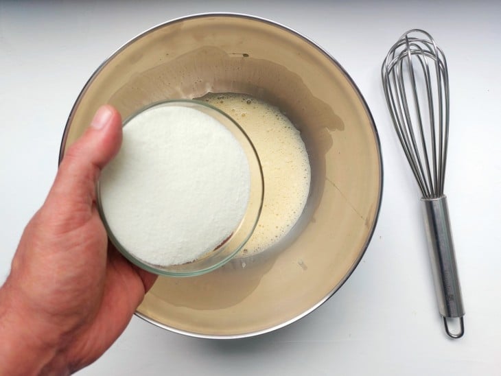 Açúcar sendo adicionado à tigela com ovos batidos.