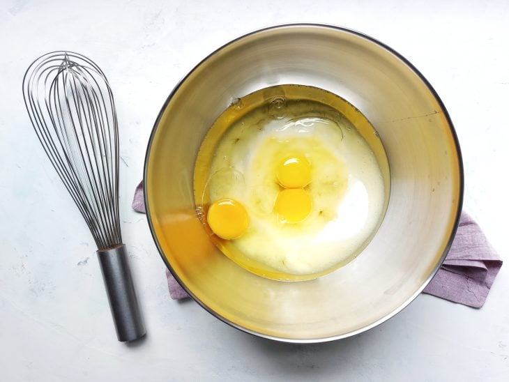 Ovos, açúcar e óleo colocados na tgela com um fouet ao lado.