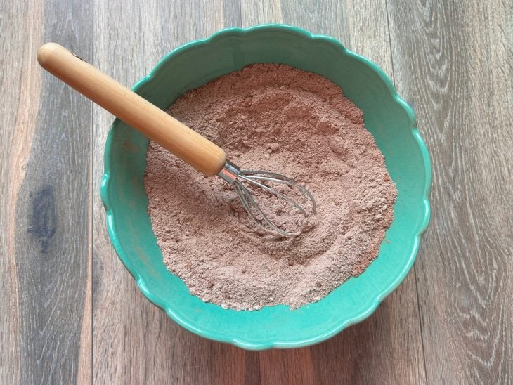 Tigela redonda com os ingredientes secos misturados (farinha de aveia, açúcar, cacau em pó, fermento em pó e sal).