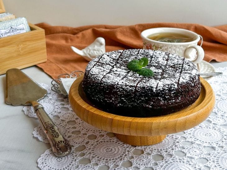 Bolo de aveia com cacau em pó assado sobre uma boleira redonda de madeira.