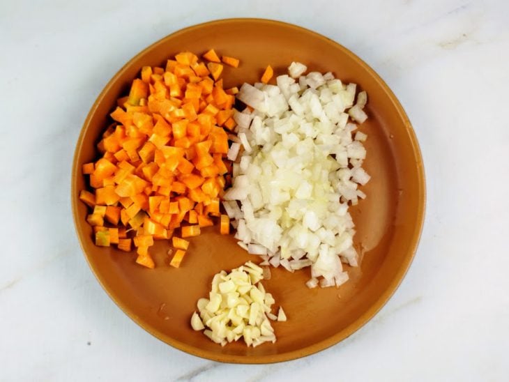 Cenoura, alho e cebola picados em um prato.