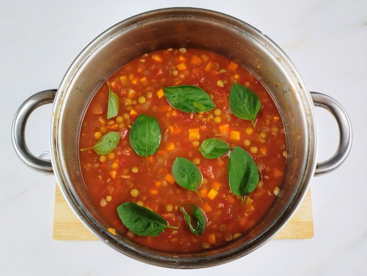 Molho de tomate caseiro e folhas de manjericão adicionados a panela.
