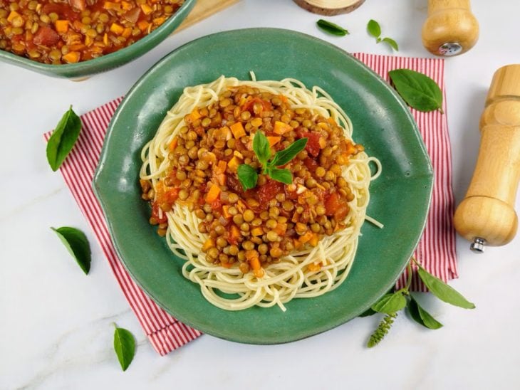 Prato com macarrão ao molho bolonhesa de lentilhas decorado com folhas de manjericão.