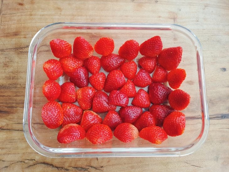 Morangos cortados ao meio e acomodados em um recipiente de vidro.