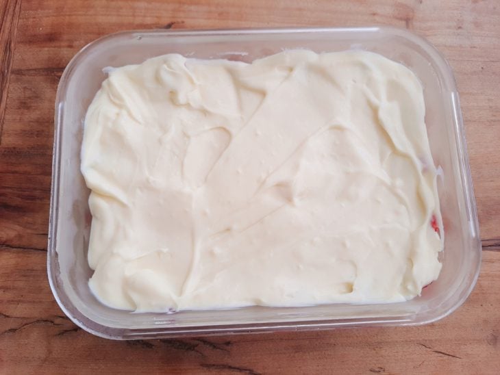 Creme despejado sobre os morangos acomodados no recipiente de vidro.