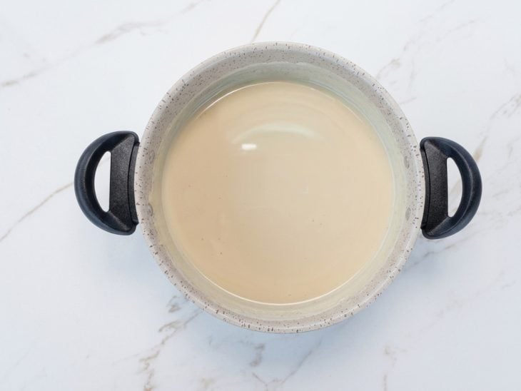 Leite condensado, leite em pó e creme de leite sendo misturados na panela ainda fora do fogo.