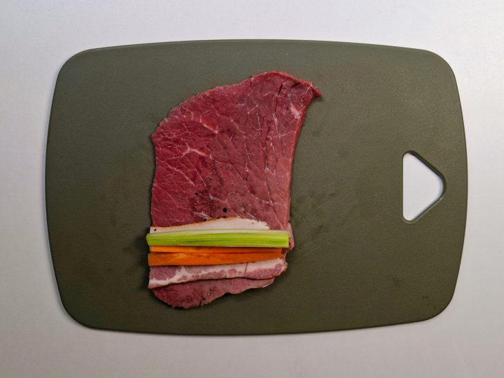 Bife recheado com bacon, cenoura e salsão sendo enrolado.