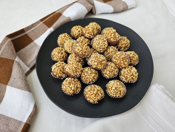 Um recipiente com vários brigadeiros de amendoim enrolados.