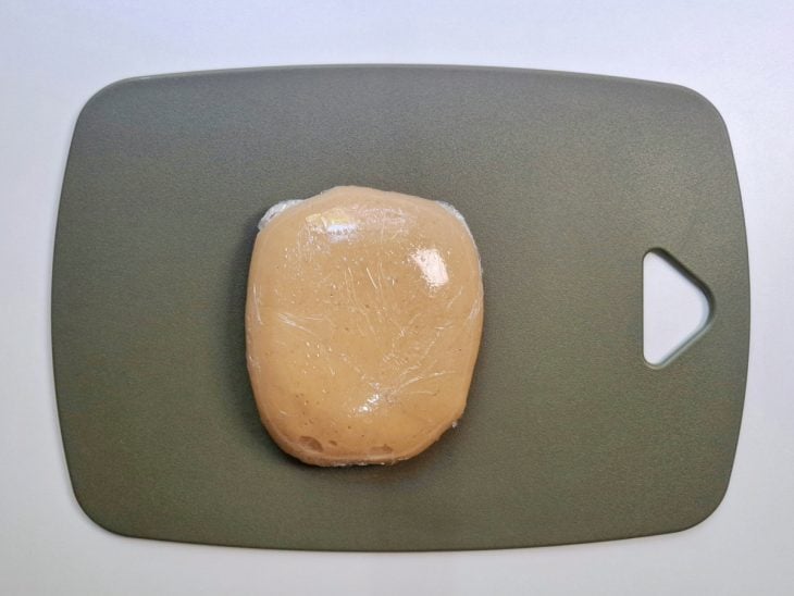 Brigadeiro enrolado em plástico filme descansando sobre uma tábua.
