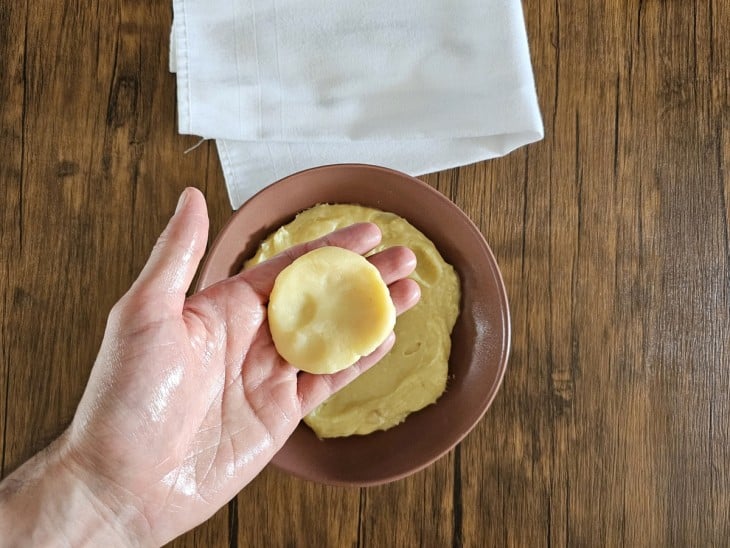 Uma mão untada com manteiga mostrando uma porção do brigadeiro aberta.