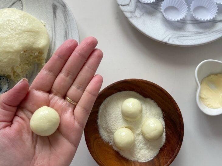 Pequenas porções da massa sendo enroladas em bolinhas com as mãos untadas.