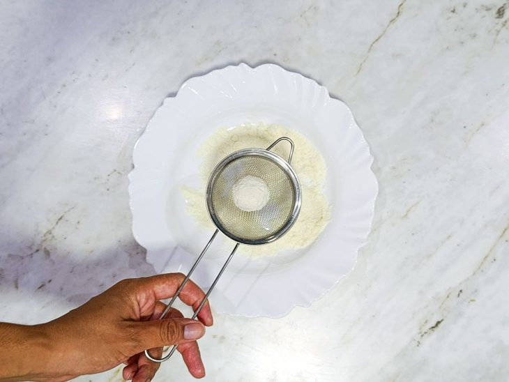 Brigadeiro passado por leite em pó numa peneira.