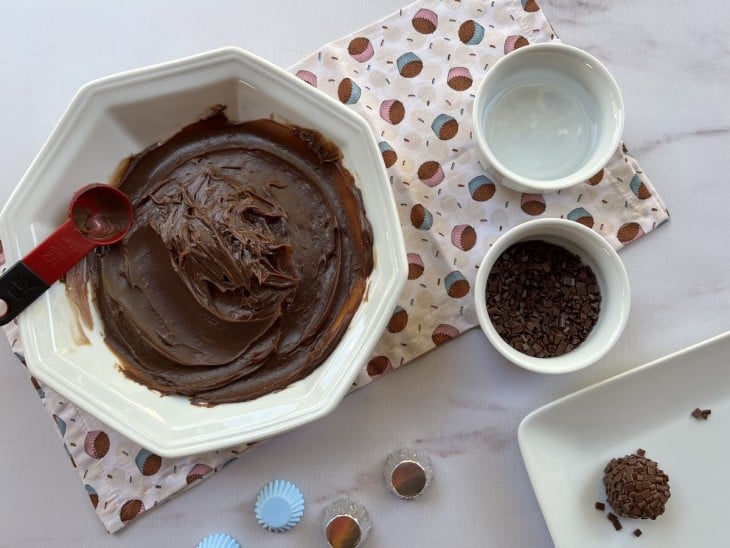 Prato com brigadeiro, recipientes com granulado e um brigadeiro pronto enrolado.