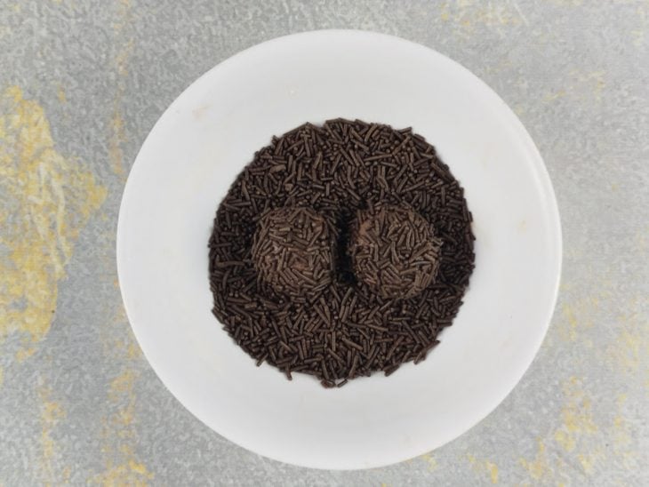 Brigadeiros sendo passados no granulado.