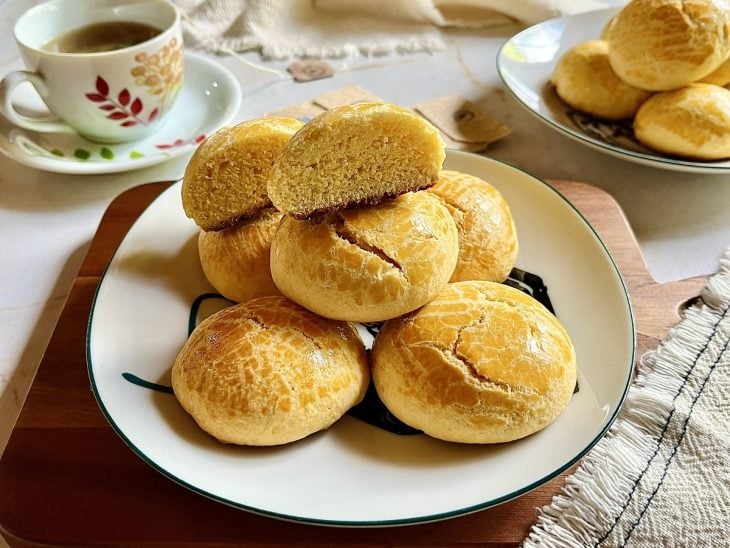 Broas prontas para consumo em um prato e uma xícara de chá ao fundo.