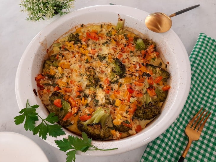 Brócolis gratinado fit pronto, com aspecto dourado e crocante, disposto em uma travessa de cor branca.