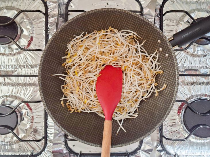 Broto de feijão sendo refogado rapidamente na frigideira.