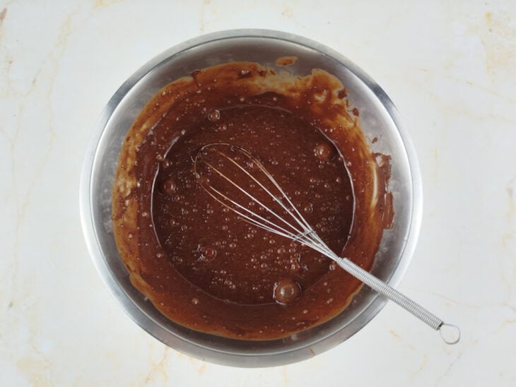 Ovos e baunilha sendo incorporados ao chocolate derretido com um fouet.