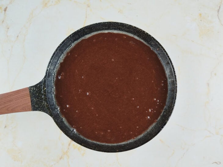 Massa de brownie sendo espalhada em uma frigideira untada.