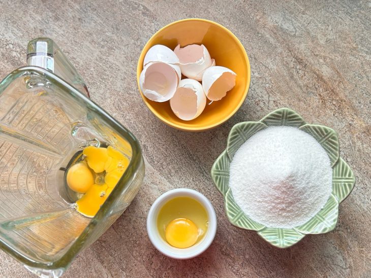 Ovos no copo do liquidificador e açúcar e óleo em recipientes distintos para serem adicionados.
