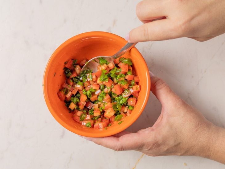 Tomates e cheiro-verde picados e misturados em uma tigela com azeite, sal e pimenta-do-reino.