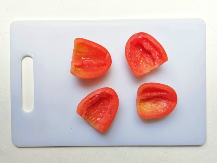 Um tomate cortado em 4 partes sem e sem as sementes.