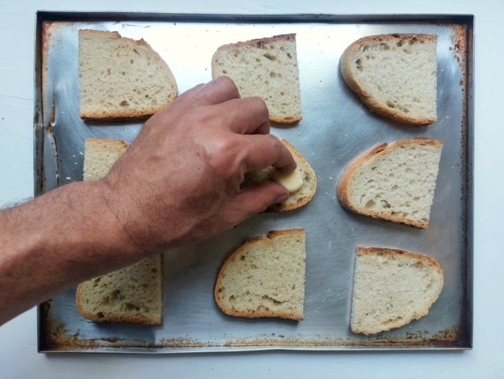 Mão esfregando um alho nas fatias de baguete.