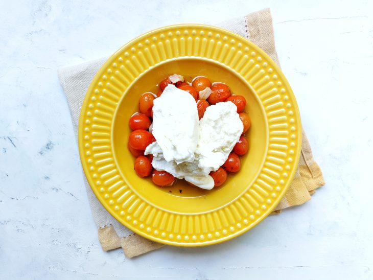 Queijo burrata por cima do tomate em um prato amarelo.