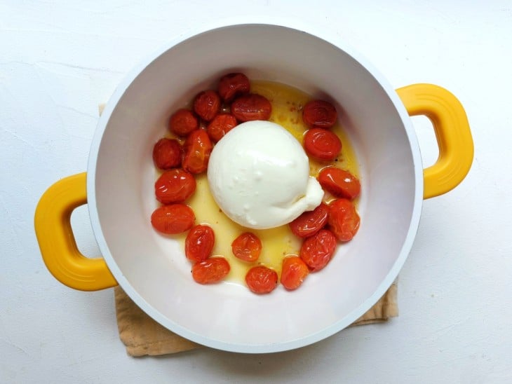 Burrata gratinada colocada no meio da panela com tomate-cereja.