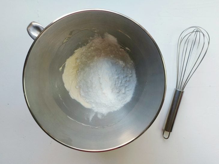 Um fouet e uma tigela contendo manteiga batida e açúcar de confeiteiro.
