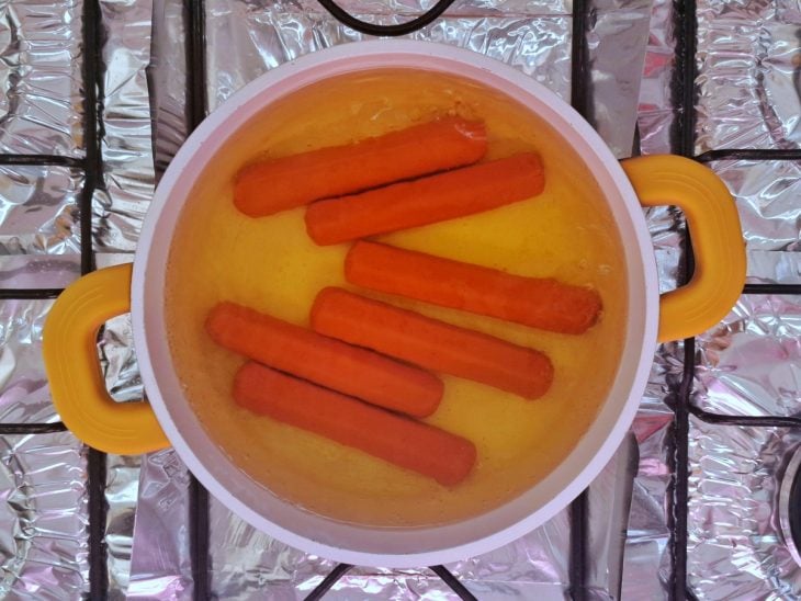 Panela com água e salsichas cozinhando.