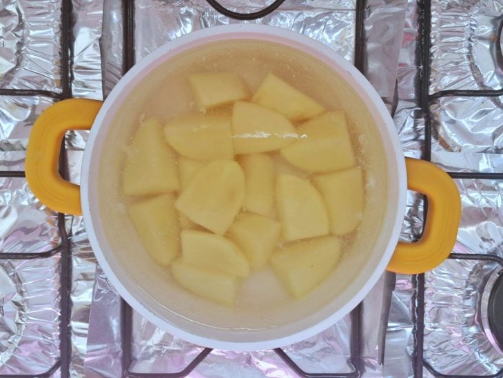 Uma panela com água e batatas cozinhando.