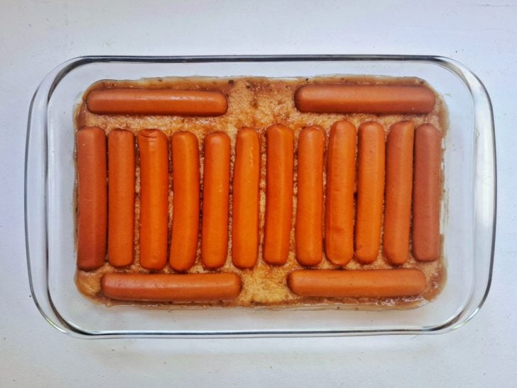 Refratário com molho, uma camada de pães e uma camada de salsicha.