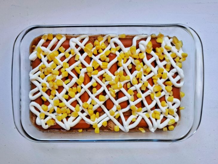 Refratário com molho, uma camada de pães, salsicha, requeijão e milho.