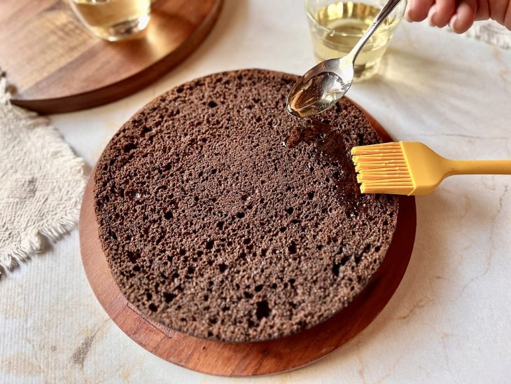 Calda de açúcar sendo espalhada sobre um bolo de chocolate.
