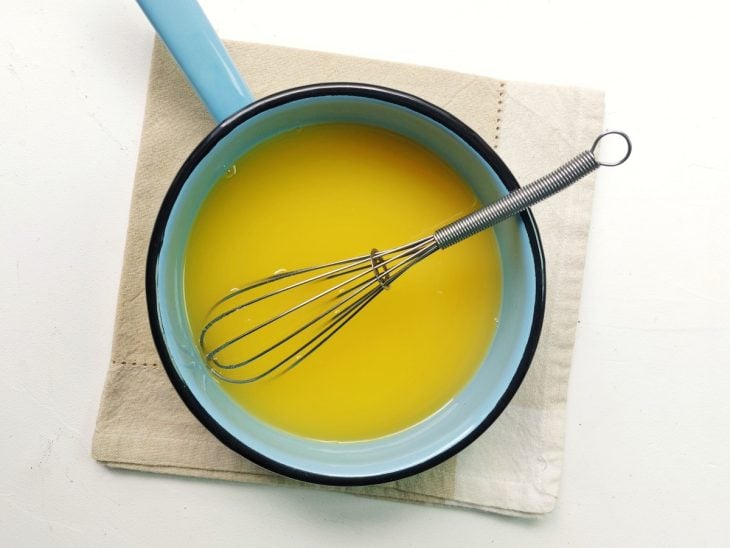 Um fouet e uma panela com suco de laranja e açúcar.